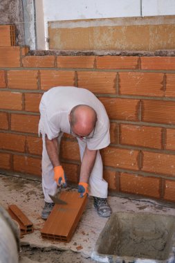 Duvarda tamir etmek için tuğla kıran bir inşaatçı..