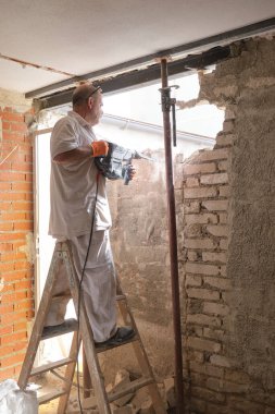 Mason yıkım çekiciyle bir ev duvarını yıkıyor..