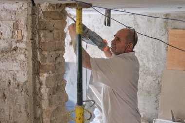 Yıkıcı çekiçli bir inşaatçı evin duvarını yıkıyor..