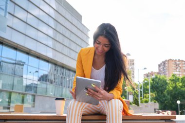 Genç Latin iş kadını açık havada bir tabletle çalışıyor..