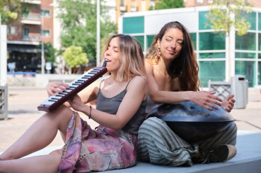 İki kadın sokakta el pençe ve melodik org çalarken gülüyor.