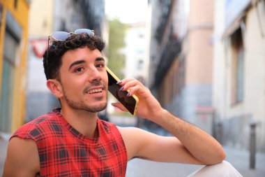 Young caucasian man with long false nails speaking on the smartphone sitting on the floor.