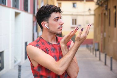 Uzun takma tırnakları olan ve kollarıyla poz veren beyaz bir adamın portresi..