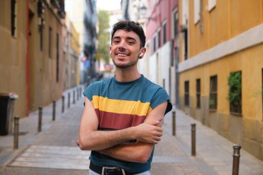 Young caucasian man with long false nails and wireless earbuds posing looking at camera and smiling at street.