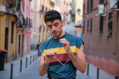 Uzun takma tırnakları olan, güneş gözlükleriyle poz veren beyaz bir genç caddeye bakıyor..