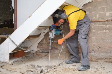 Kafkasyalı genç inşaat işçisi bir kaya matkabıyla evin zeminini kırıyor..