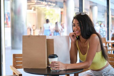 Genç Latin bir kadın alışverişe gittikten sonra açık bir kafede kahve içiyor..