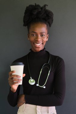 Steteskoplu gülümseyen Afrikalı kadın doktor portresi ve siyah arka planda bir fincan kahve. Stüdyo çekimi.