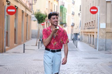 Uzun takma tırnaklı genç beyaz adam yürürken telefonuna ses kaydediyor..