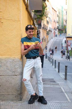 Uzun takma tırnakları olan beyaz bir adam duvara karşı akıllı telefon kullanıyor..