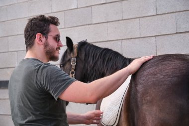 Genç Latin adam atına eyer battaniyesini giydirip ata binmeden önce onu okşadı..