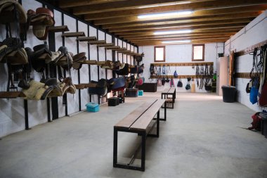 Sürme raptiyeli depo odası: duvara asılı at eyerleri ve dizginleri.