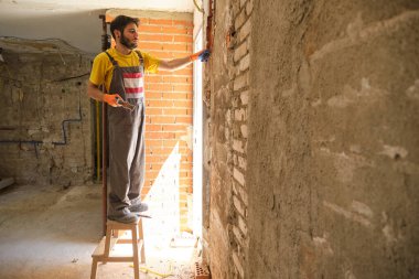 Kafkasyalı genç bir inşaat işçisi çekiç ve keskiyle bir evin duvarını yıkıyor..