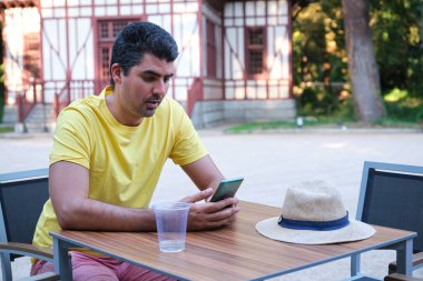 Akıllı telefonu kullanan bir turist yaz tatili terasında oturuyor. Şapkalı..