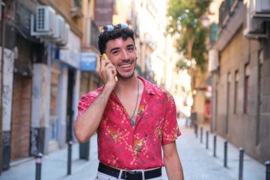 Uzun takma tırnakları olan, gülümseyen ve akıllı telefondan konuşan beyaz bir genç..