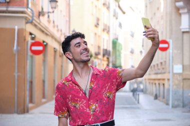 Uzun takma tırnaklı beyaz bir adam akıllı telefonuyla sokakta selfie çekiyor..