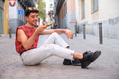 Uzun takma tırnaklı genç beyaz adam yerde oturan akıllı telefondan ses kaydını kaydediyor..