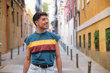 Uzun takma tırnakları olan, gülümseyen ve caddede bir tarafa bakan beyaz bir genç..