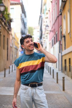 Uzun takma tırnaklı, beyaz, genç bir adam şehrin caddesinde akıllı telefondan gülümseyip konuşuyor..