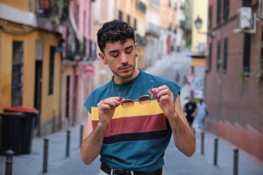 Uzun takma tırnakları olan, güneş gözlükleriyle poz veren beyaz bir genç caddeye bakıyor..