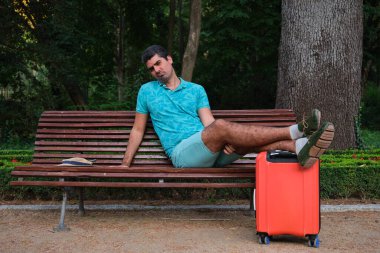 Turist bavul ve hasır şapkayla bankta poz veriyor..