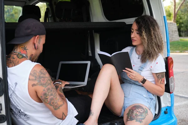 Young tattooed couple smiling, reading and working in the back of the van.