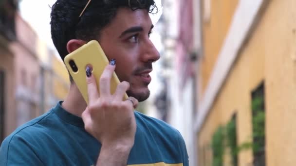 Молодой кавказский мужчина с длинными фальшивыми ногтями, улыбающийся и разговаривающий по телефону. — стоковое видео