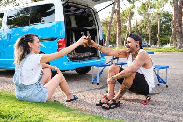 一对纹身的年轻夫妇在面包车旁边用啤酒瓶和狗一起举杯. — 图库照片