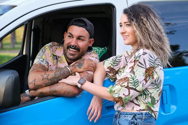 Young tattooed couple smiling with their van.