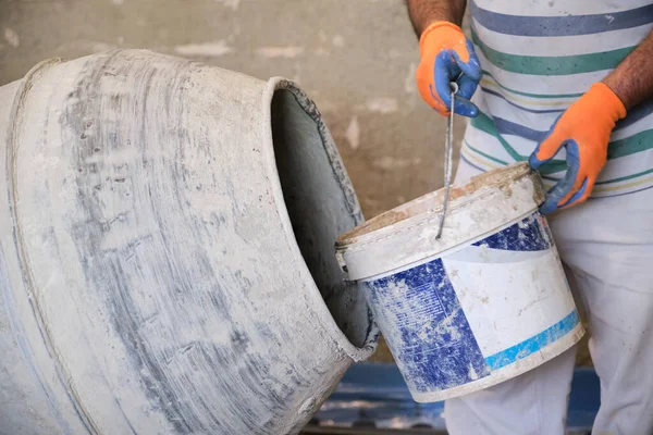 Bouwvakker met een emmer in zijn handen ladingen een betonmixer. — Stockfoto