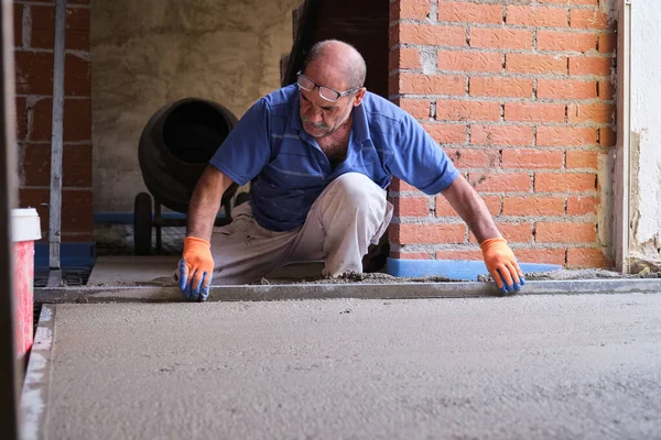 İnşaat işçisi, parlayan zeminin üstündeki betonu düzleştiriyor..