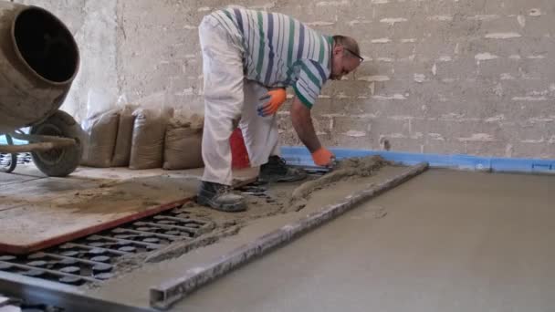 Trabalhador da construção civil espalhando concreto acima do radiante sistema de piso radiante. — Vídeo de Stock