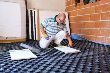 Yeraltı ısıtma sistemi kurulmadan önce bir bant ile ölçüm yapan işçiler.