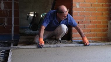 İnşaat işçisi, parlayan zeminin üstündeki betonu düzleştiriyor..