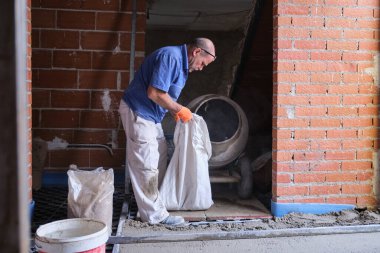 İnşaat işçisi beton karıştırıcıya kum torbası yüklüyor..