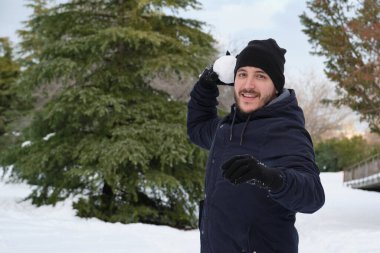 Genç beyaz bir adam parkta kartopu atmaya hazır..