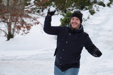 Genç beyaz bir adam parkta kartopu atıyor..