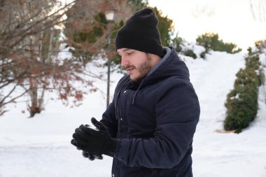 Genç beyaz bir adam parkta kartopu yapıyor..