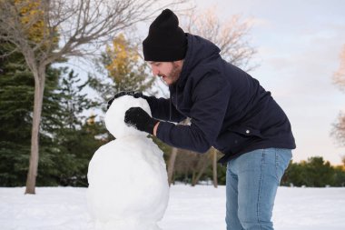 Young caucasian man making a snowman. clipart