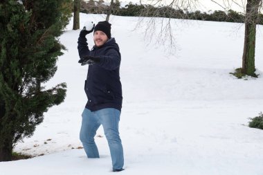 Genç beyaz bir adam parkta kartopu atmaya hazır.