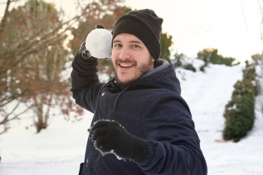 Genç beyaz bir adam parkta kartopu atmaya hazır.