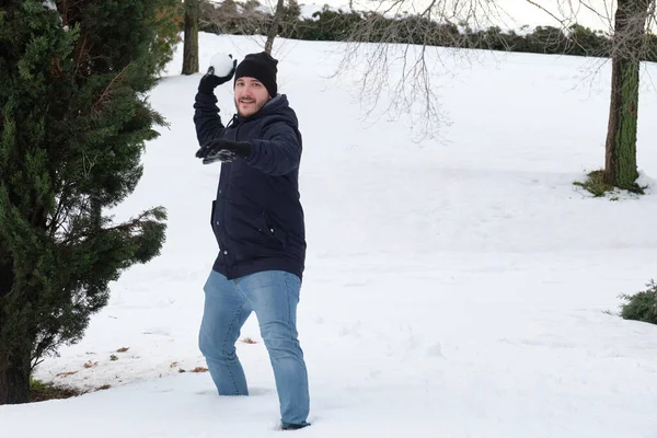 Genç beyaz bir adam parkta kartopu atmaya hazır.