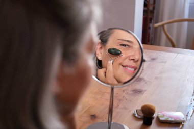 Olgun bir kadın cilt hastalığını iyileştirmek için evde yüz masajı için yeşim bir silindir kullanıyor.