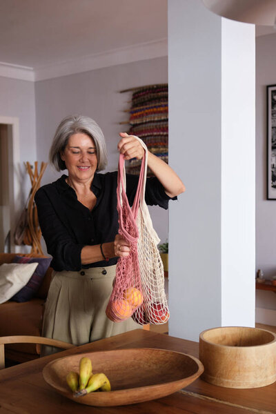 Senior woman holding a reusable shopping bag with peaches, promoting sustainable living and eco conscious choices
