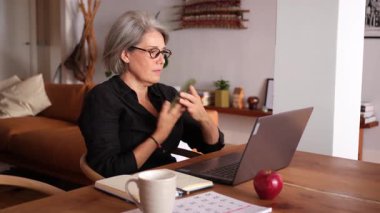 Evde cep telefonu kullanan olgun bir kadın, balkon kapısının yanındaki tahta zeminde çıplak ayakla oturuyor.
