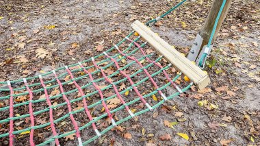 Kahverengi sonbahar yaprakları ve meşe palamudu ile kaplı yerde dinlenen renkli halat tırmanma ağı