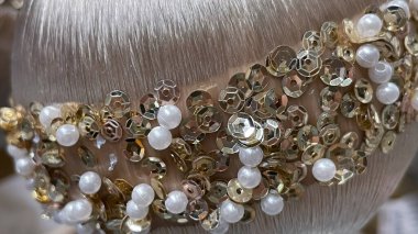 Yumuşak, pürüzsüz desenli bir yüzeyde altın pullar ve beyaz inciler.