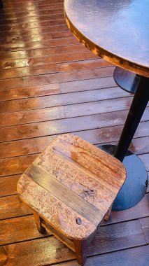 Su damlacıkları ve ıslak ahşap zeminde sıcak yansımalar ve bir masanın yanındaki kır evindeki tabure.