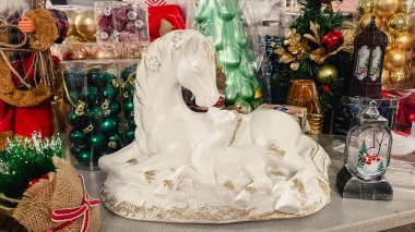 Beyaz seramik at ve tay heykeli Noel süsleri ve hediyelerle çevrili bir mağazanın rafında.