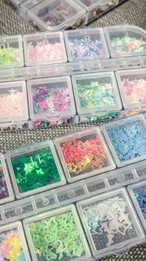 Çeşitli pastel kelebeklerin ve yıldız pullarının üst görüntüsü çok bölmeli bir zanaat depolama organizatöründe..